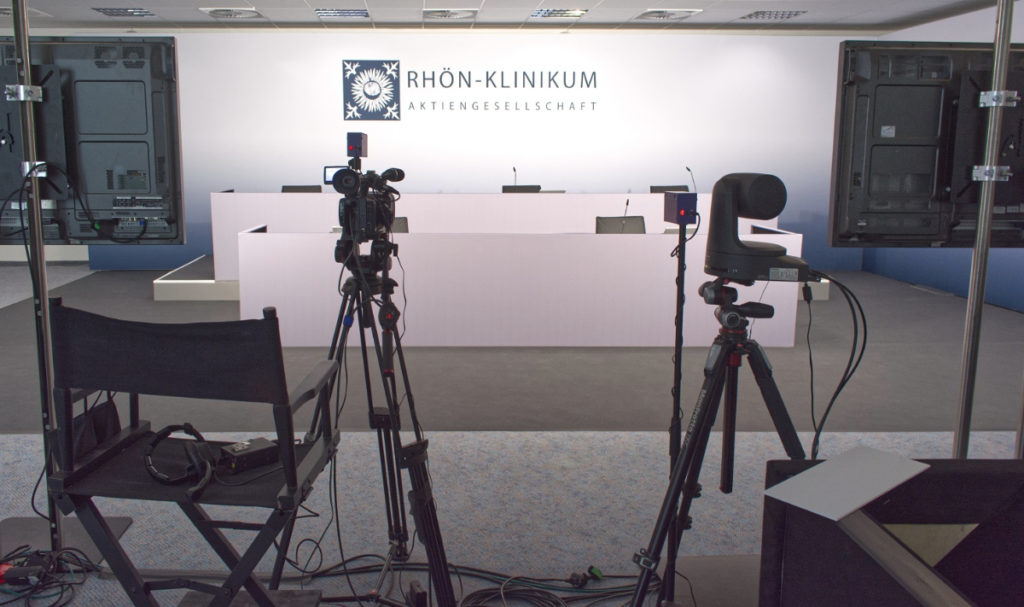 blick auf den konferrenzraum mit kamera und hintergundwand mit firmen logo des veranstalters
