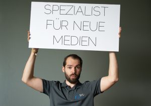 neuer mitarbeiter von concert media, haelt schild mit spruch, spezialist fuer neue medien